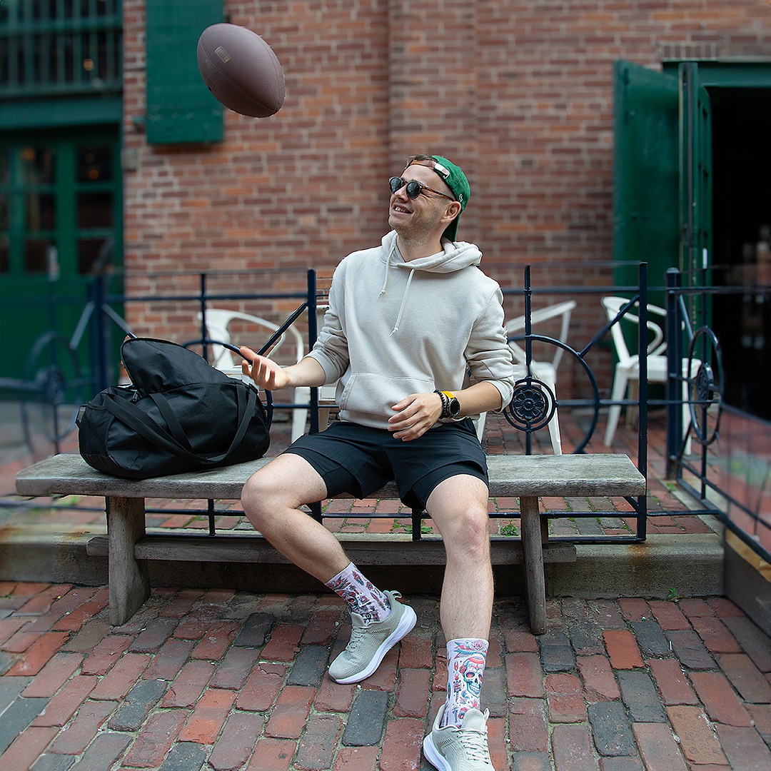 Person throwing a football upward while sitting down wearing custom socks
